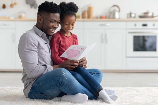 Smiling Black Father And Daughter Engaged In Reading A Card Together, Enjoying Quality Time At Home In A Cozy Setting. Strong Family Bonding Moment Full Of Joy And Happiness, Family Concept.