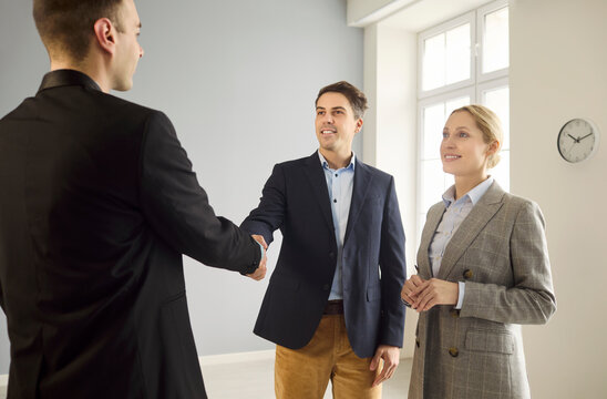 Realtor clients couple handshake agreement contract property. Cheerful buyers greet an agent in a sunny apartment to review mortgage options, pricing and timelines. Clear deal concept for all.