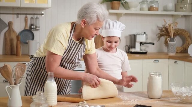 Happy family in kitchen. Grandmother and granddaughter child cook in kitchen together. Grandma teaching kid girl roll out dough bake cookies. Household teamwork helping family generations concept