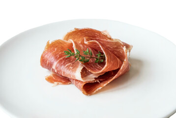 Fototapeta premium Thinly sliced cured pork meat folded on a white plate with fresh herbs