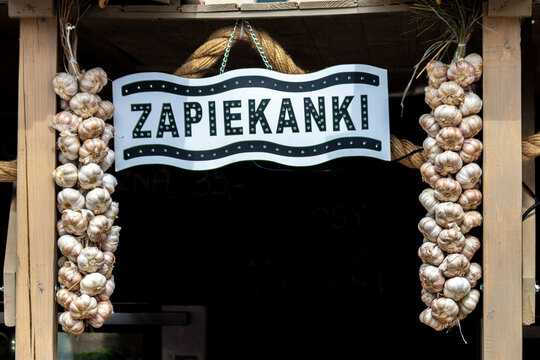 Zapiekanki kiosk sign flanked by hanging garlic braids at street stall