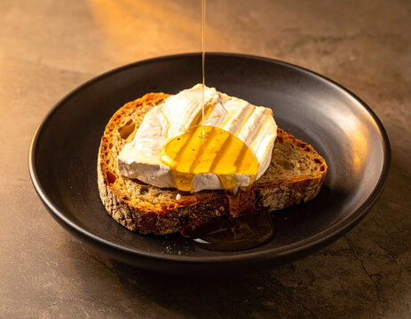 Sliced artisan bread with melted Afuega'l pitu cheese and a drizzle of honey on a dark ceramic plate.