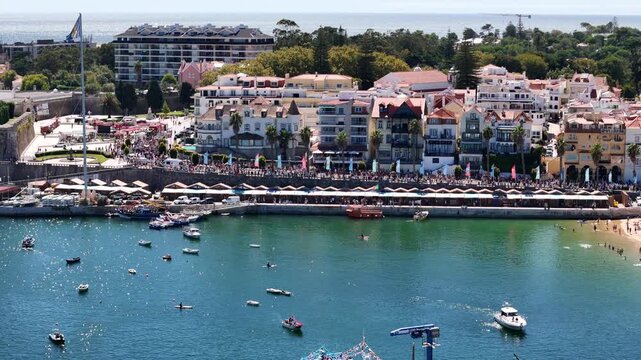 Cascais, Portugal - 30 August 2026: Aerial view of the bustling harbor and waterfront with numerous boats, historic buildings, and people enjoying the sunny day.
