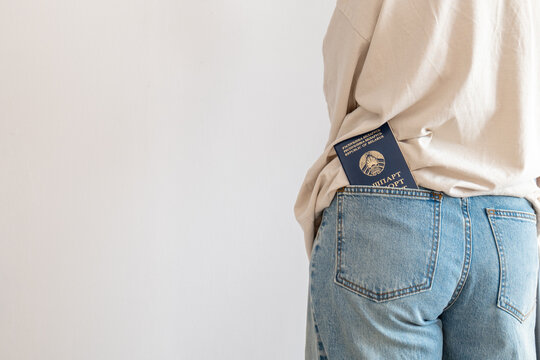 Person with passport holding passport in pocket, in indoor plain background, with passport, jeans, shirt, from a side view perspective, with blue, beige accents, and neutral mood, nearby objects.