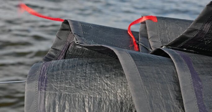 A black folded carbon sail with red ribbons lies on the side of a sailing boat when moving