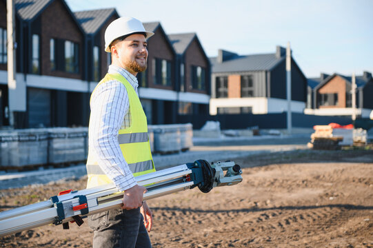 Surveyor engineer carrying leveling instrument on construction site