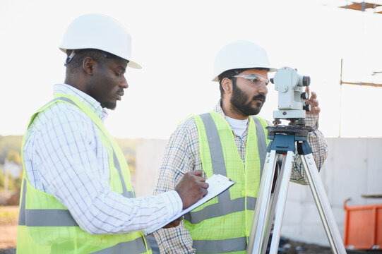 Engineers surveying construction site with leveling instrument and notes