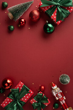 Red and green Christmas gifts with ornaments and a nutcracker on a festive red vertical background
