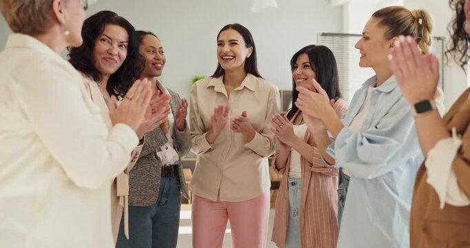 Women team share applause in a meeting. They stand in a circle clapping for a colleague, signaling recognition and a positive office culture. Clear message of teamwork, support, and success.
