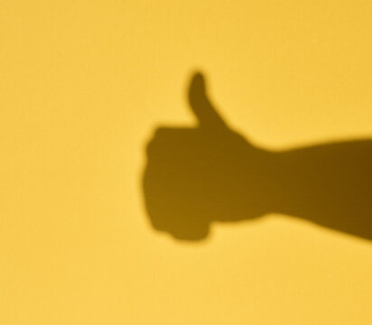 A shadow of a hand with a thumbs up gesture on a yellow background. A gesture of approval.