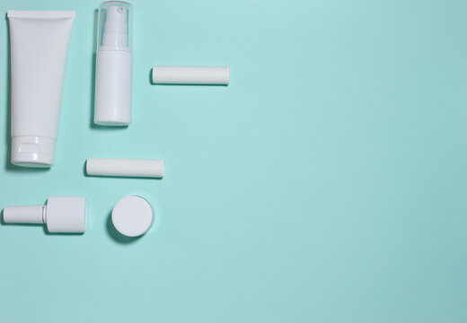 Set of white cosmetic packaging, tubes, and bottles on a turquoise background.