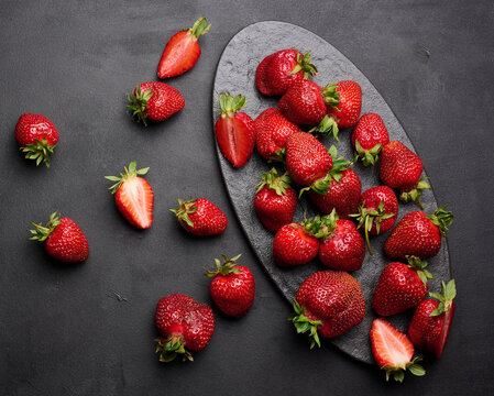 Fresh ripe strawberry on a dark background, whole berries and slices on a stone board.