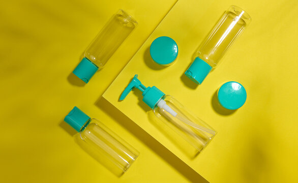 A set of transparent cosmetic plastic bottles and jars with turquoise lids on a yellow background