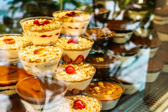 Assorted layered desserts in clear plastic cups displayed in a refrigerated bakery case