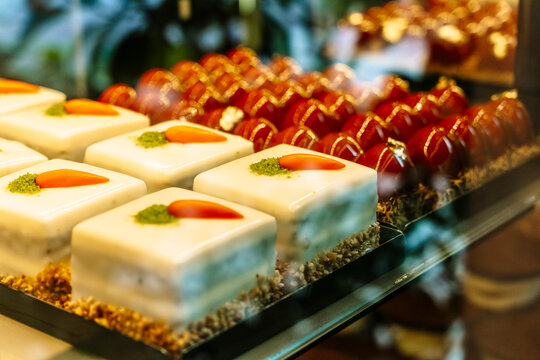 Assorted gourmet pastries with white glaze and red mirror-glaze sweets in a bakery showcase