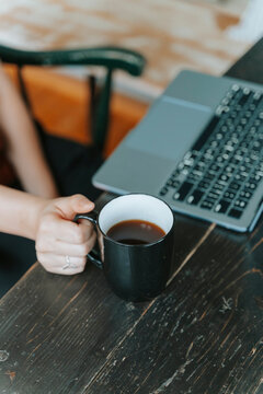 Person working on a laptop while holding a cup of coffee on a dark wooden table