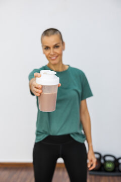 Smiling sportswoman offers protein shake after workout in gym