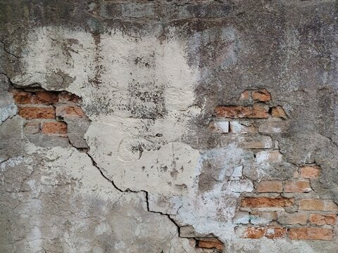 Old cracked stucco wall with visible red brick layers texture. Distressed weathered concrete and brickwork background.