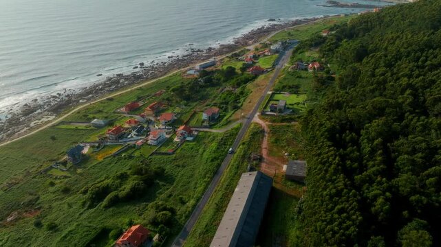 Peaceful aerial perspective of a charming coastal neighborhood in A Guarda, Spain, where sun-drenched homes are nestled between a lush, verdant forest and the rhythmic, sparkling Atlantic coastline
