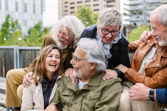 Multi-ethnic seniors laughing and relaxing together in an urban park, enjoying friendship, active retirement, and carefree moments of connection and well-being outdoors