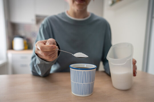 Woman adds white sugar to coffee with spoon, illustrating habitual sweetening, sugar dependence and difficulty reducing added sugar despite efforts to change unhealthy daily eating habits.