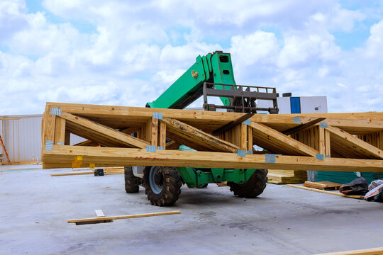 Telehandler forklift lifts heavy wooden beams at construction site workers are present nearby.