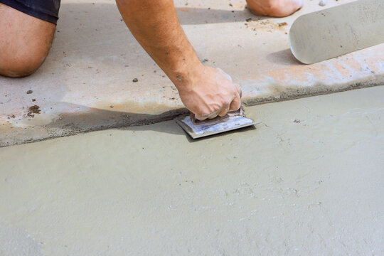 Builder levels wet concrete on construction site using trowel wearing gloves.