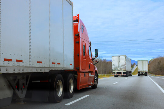 Two trucks move along an American highway in rural area, with trees lining roadside.