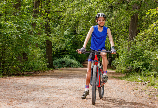 Happy teenage boy riding mountain bike along sunny forest trail