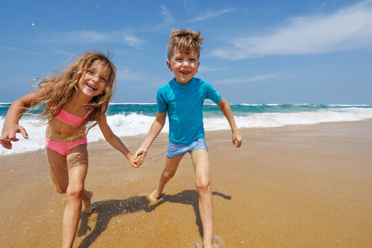 Children running laughing together along a sunny beach shoreline