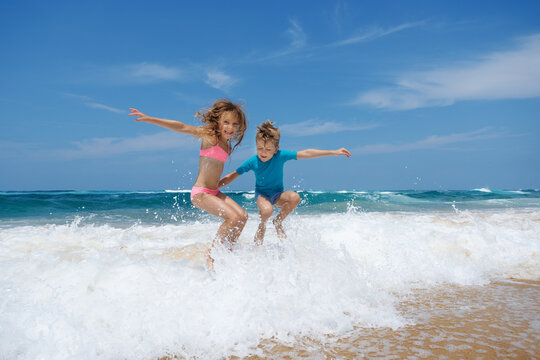 Happy kids jumping through ocean surf at sunny beach together
