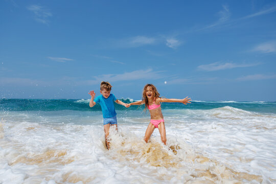 Boy and girl have fun running in ocean waves on sunny beach
