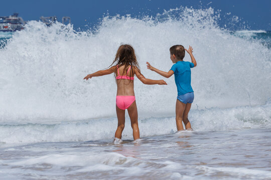 Children facing breaking ocean wave at shoreline in daylight