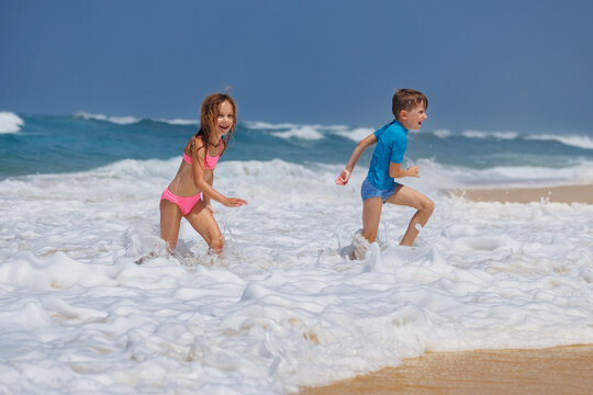 Children running splashing through ocean surf along sandy beach