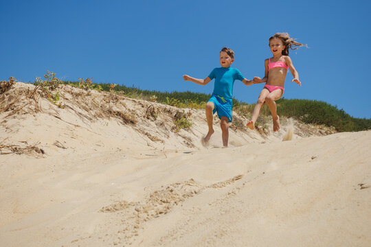 Kids have fun running down a sandy dune at the beach outdoors