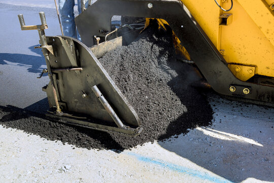 Workers operate paving machine to spread asphalt on road surface in neighborhood setting.