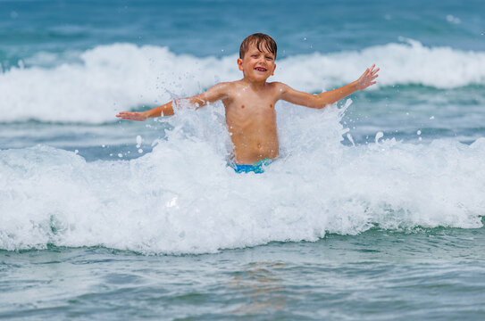 Boy have fun splashes through ocean waves at beach in summer