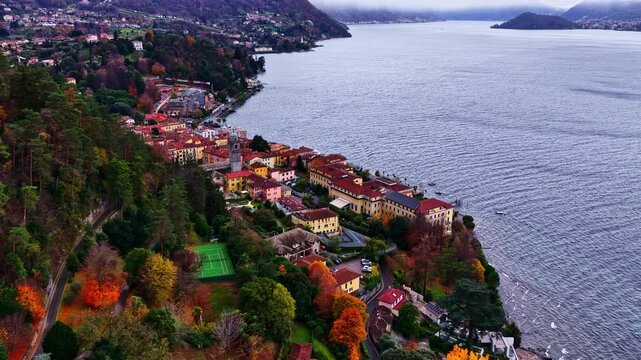 Aerial view of the historic town of Bellagio with colorful buildings, lush autumn trees, and a tennis court along the shore of Lake Como in Bellagio, Lombardia, Italy.