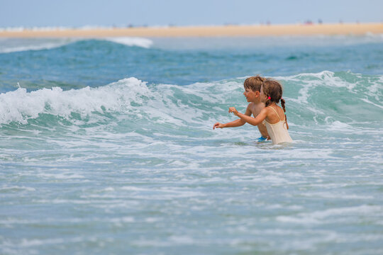 Two children have fun playing in ocean waves near a sandy beach