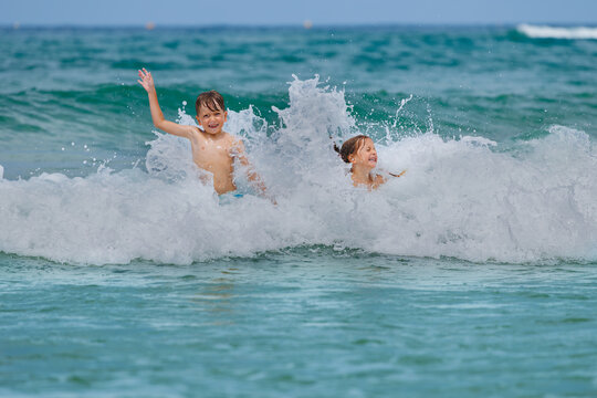 Children happily playing in ocean waves at beach during summer