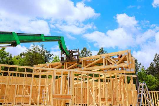 Workers are placing wooden joins frame beams on building frame with crane while construction area