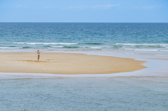 Happy woman stand with arms out on a small sandy ocean island