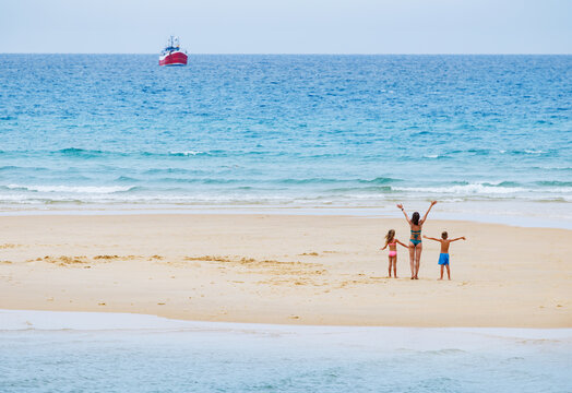 Family jumping on sandy island, making waving sign to a boat