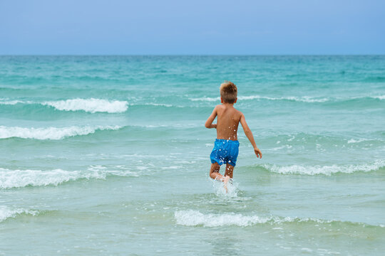 Child runs Into turquoise sea through shallow breaking waves