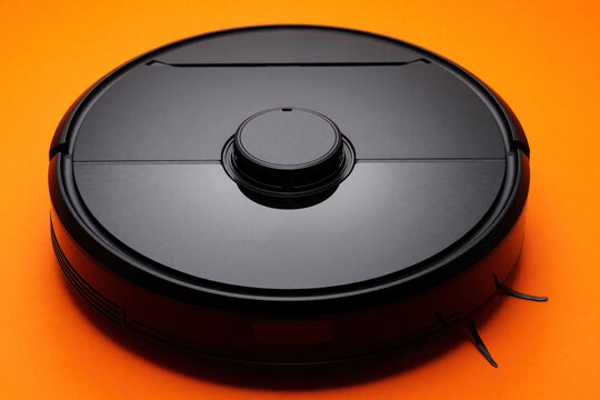 Black robotic vacuum cleaner sits on bright orange background. Modern appliance uses tech for automated home cleaning convenience and efficiency. Future tech for tidiness.