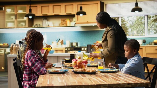 African American woman pours orange juice at breakfast table