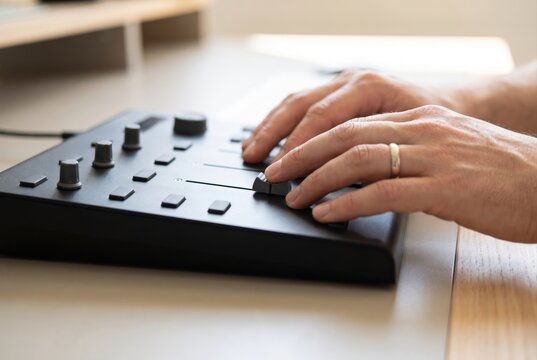 Hands adjusting knobs and sliders on a modern dark audio MIDI controller