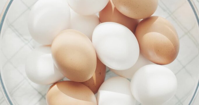 White and brown chicken eggs in a transparent bowl on a stylish napkin.