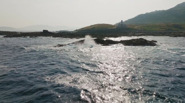 Peaceful aquatic perspective of a distant lighthouse standing watch over rocky, sun-dappled coastal waters, evoking a sense of tranquil isolation and timeless maritime beauty
