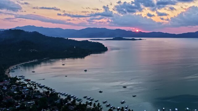 Aerial view of Port Barton Beach at sunset with boats anchored in the bay and mountains in the distance in Mimaropa, Philippines.